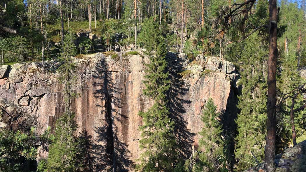 Kallioseinämä, jonka tasanteella on kaide. Ympärillä on metsää.