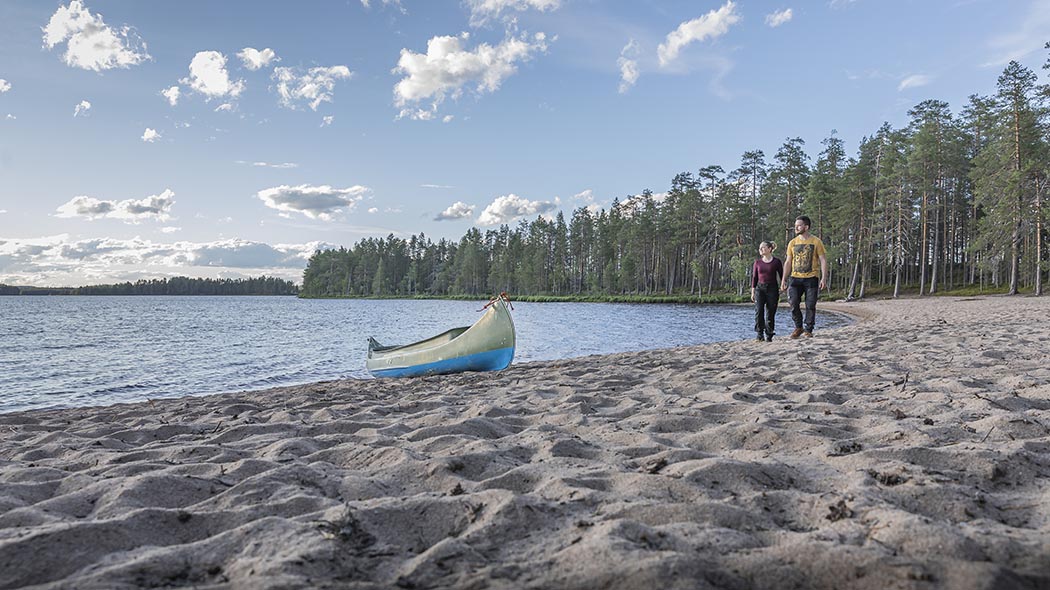 Kaksi retkeilijää kävelee pitkällä, kaareutuvalla hiekkarannalla.