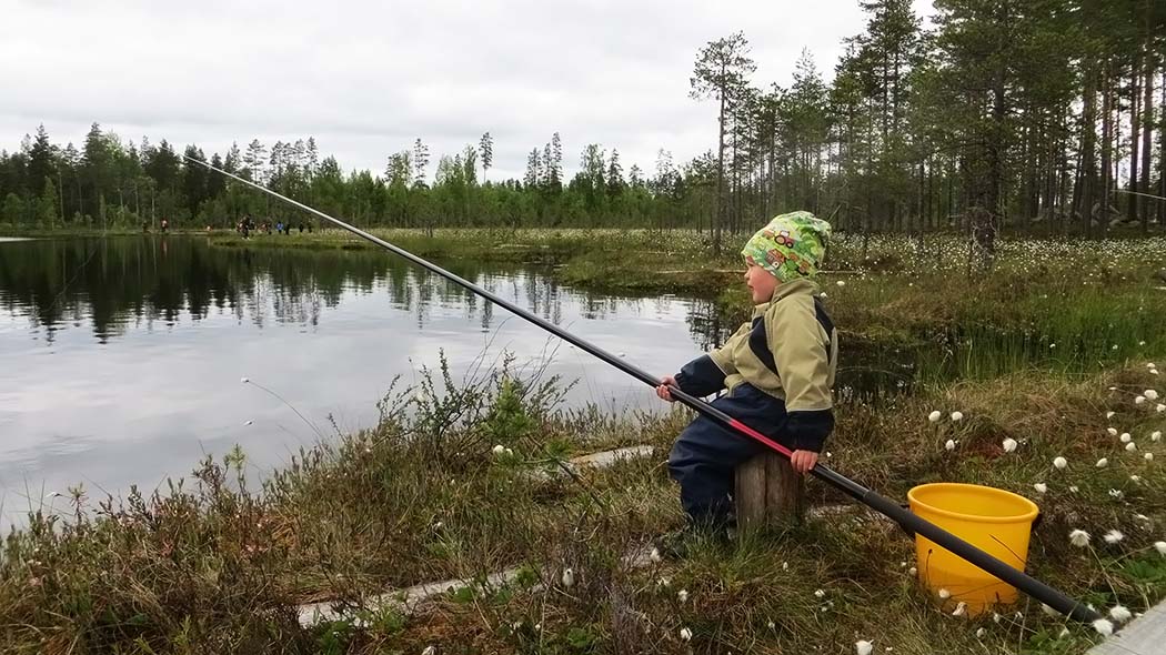 Lapsi istuu onki kädessä lammen rannalla.