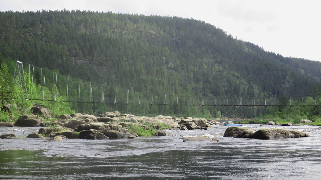 Vuolaasti virtaava joki, jonka rannat ovat kiviset ja maa nousee molemmilla puolilla. Joen yli menee kapea teräksestä tehty riippusilta.