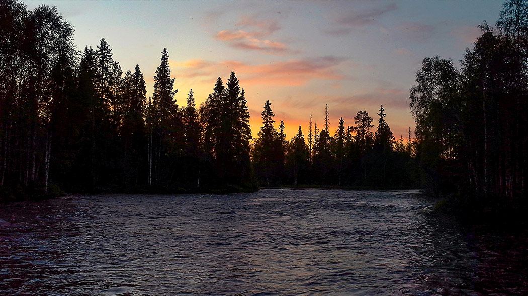 Simojoen maisemia auringonlaskun aikaan. Rannoilla kasvavien puiden siluetit erottuvat auringonlaskua vasten.Illan hämyä Simojoen Saarikoskella. Kuva: Juha Paso.