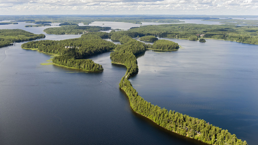 Lentokuvaa järvimaisemasta. Maisema näkyy kaukaisuuteen. Metsä ja vesi vuorottelevat. Kuvassa on pitkä ja kapea harjumuodostuma.