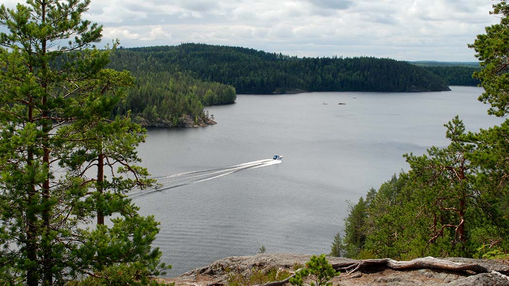 Ylhäältä linnavuorelta avautuva järvimaisema. Kesäisellä järvellä moottorivene.