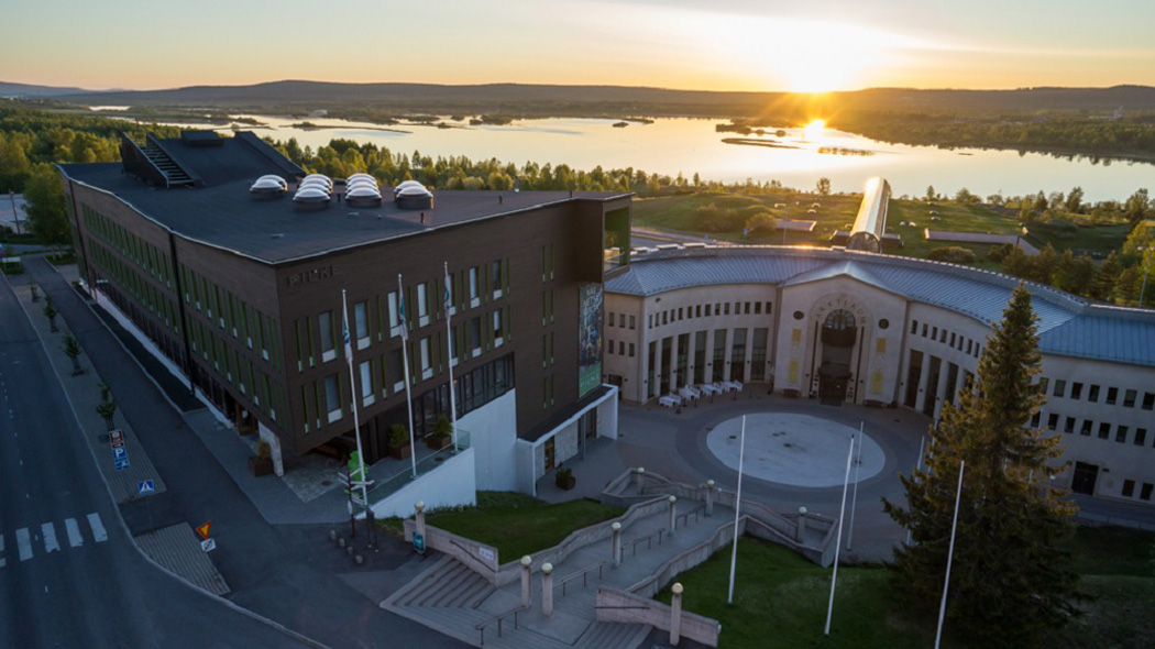 Kaksi suurta rakennusta joen rannalla keskikesän yöttömässä yössä. Rakennusten seinäilä lukee Pilke ja Arktikum. Kuva: Flatlight Creative House