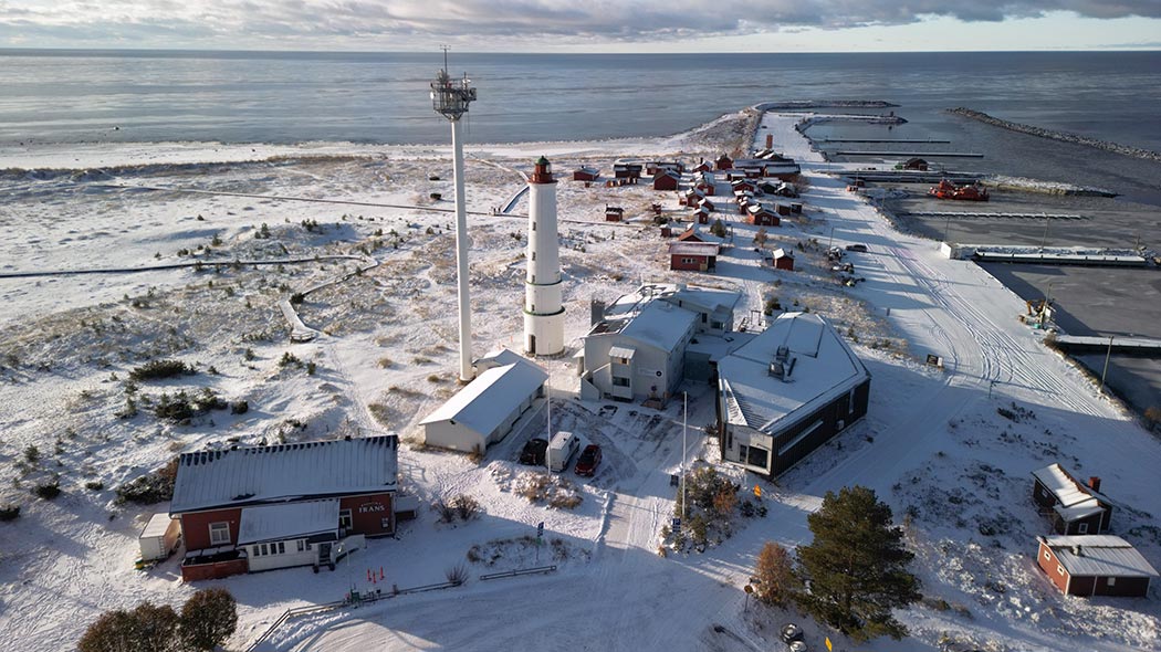 Ilmakuva Hailuodosta. Punaisia mökkejä ja majakka seisovat hiekkaisella niemellä. Ympärillä on sinistä merta.