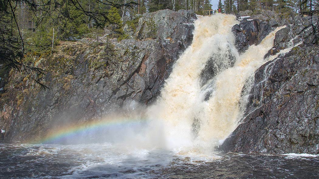 Korkea kuohuva koski. Ihmisiä kallioseinämän päällä.