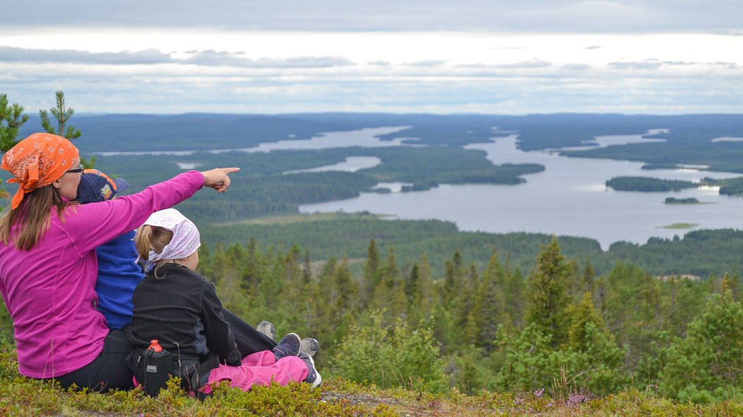 Vaaran päällä istuu kahden lapsen kanssa aikuinen, joka osoittaa lapsille kaukana olevaa kohdetta sormellaan.