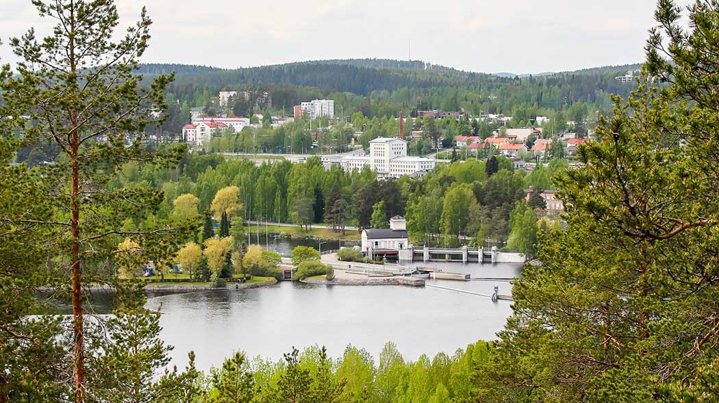 Etualalla puiden latvoja, joiden välistä avautuu järvi ja kaupunkimaisema.